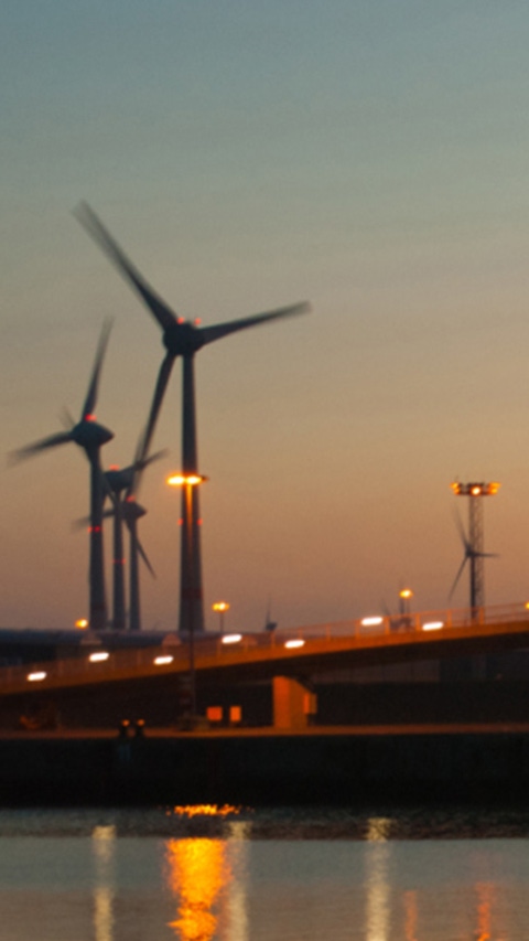 Landscape view of a bridge by the water with windmills during sunset 